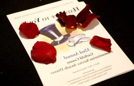 The program for the 2022 Garfield County Humanitarian Awards on a black tablecloth and covered with red rose petals.